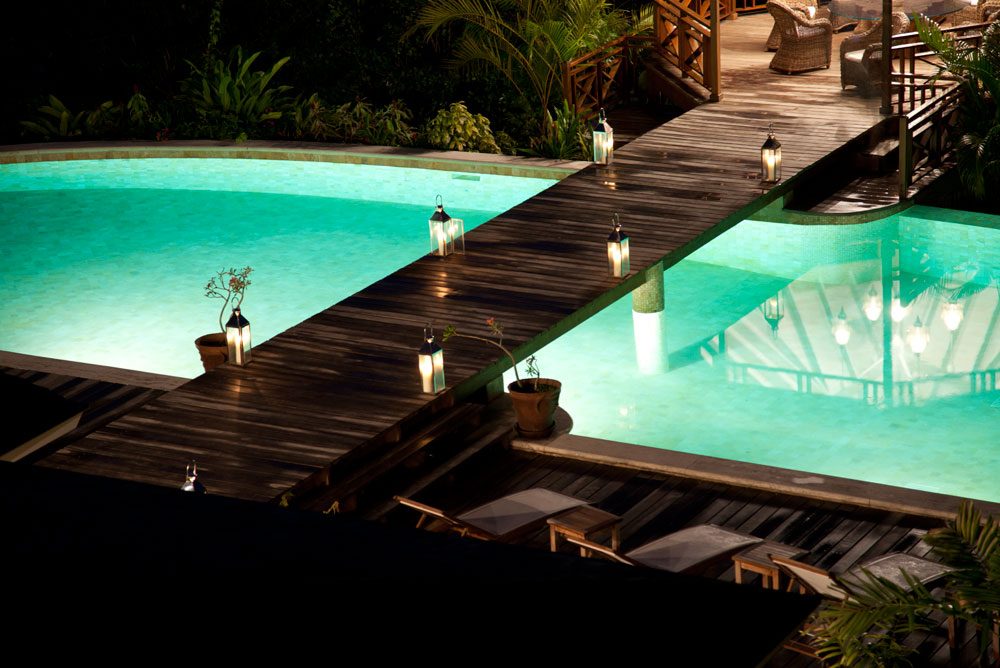 Lantern-lit wooden walkway across a turquoise pool in St. Lucia