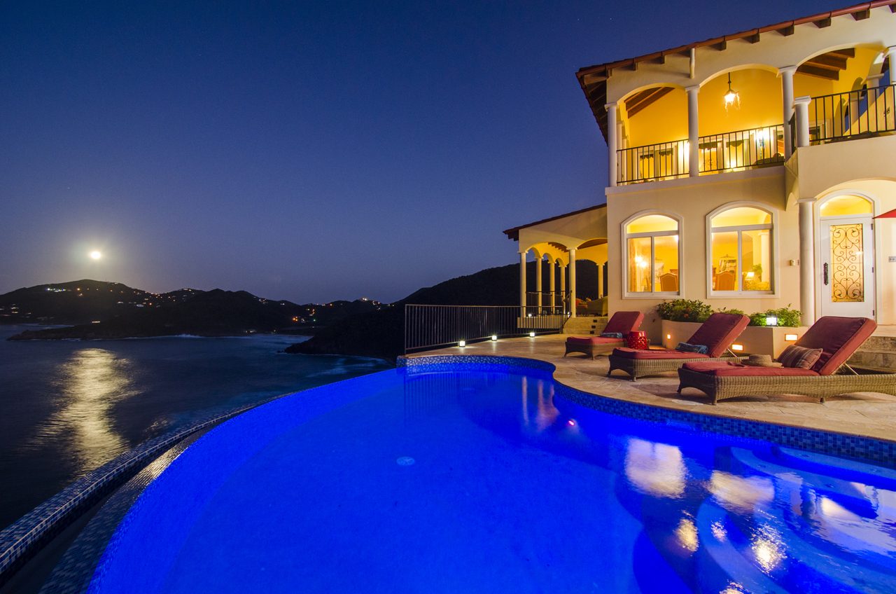 An infinity pool and villa terrace overlooking the water at dusk in Tortola